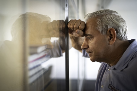 Man resting his head on his hand up against glass wall