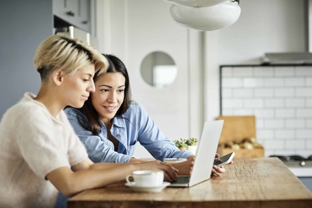 Two women sitting in kitchen looking at a laptop together