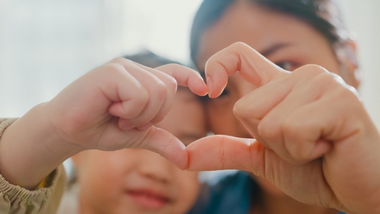 woman and young child holding up their fingers to form a heart
