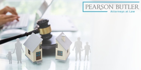 Miniature house and family figurines being divided by a judge's gavel.