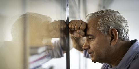 Man resting his head on his hand up against glass wall