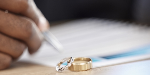 person signing documents with wedding rings in the foreground