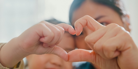 woman and young child holding up their fingers to form a heart