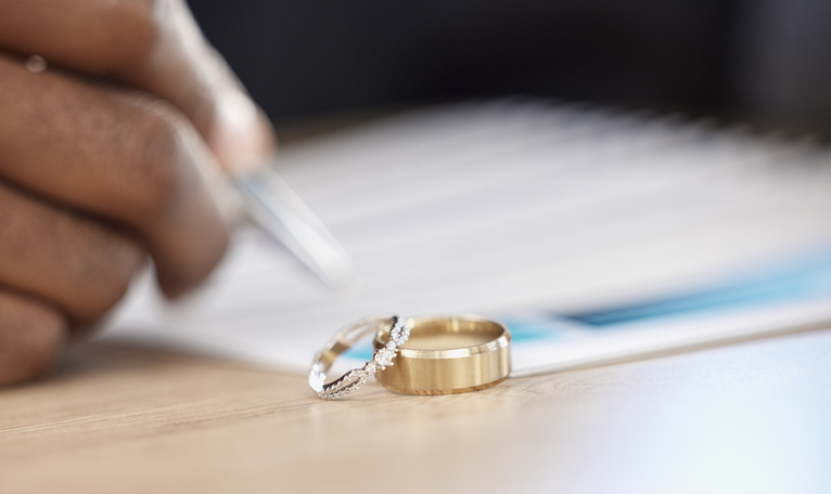 person signing documents with wedding rings in the foreground