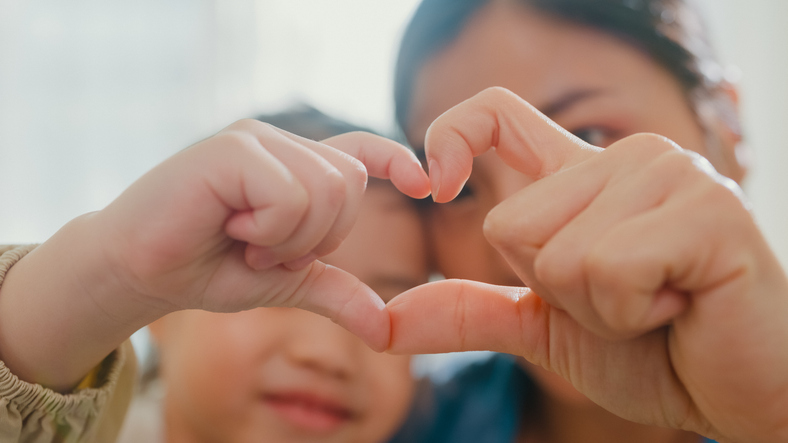 woman and young child holding up their fingers to form a heart